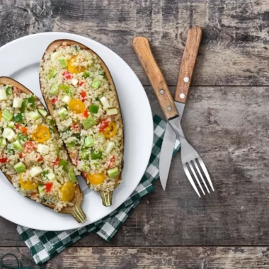 Quinoa-stuffed eggplant on a plate with a knife and fork.