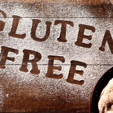 The words gluten-free written in flour with a loaf of gluten-free bread on the side.