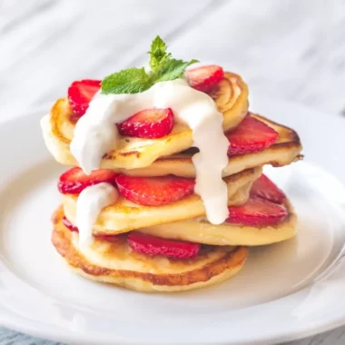 Gluten-free vanilla pecan pancakes on a plate garnished with whipped cream and fresh strawberries.