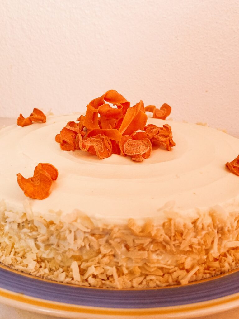 Gluten-free carrot cake decorated with sugar-free cream cheese frosting and dehydrated carrot chips on a plate.