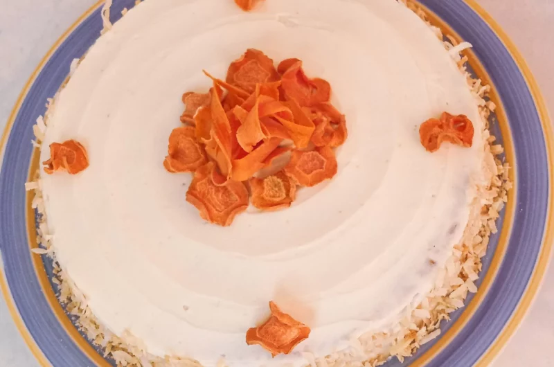 Gluten-free carrot cake decorated with sugar-free cream cheese frosting and dehydrated carrot chips on a plate.