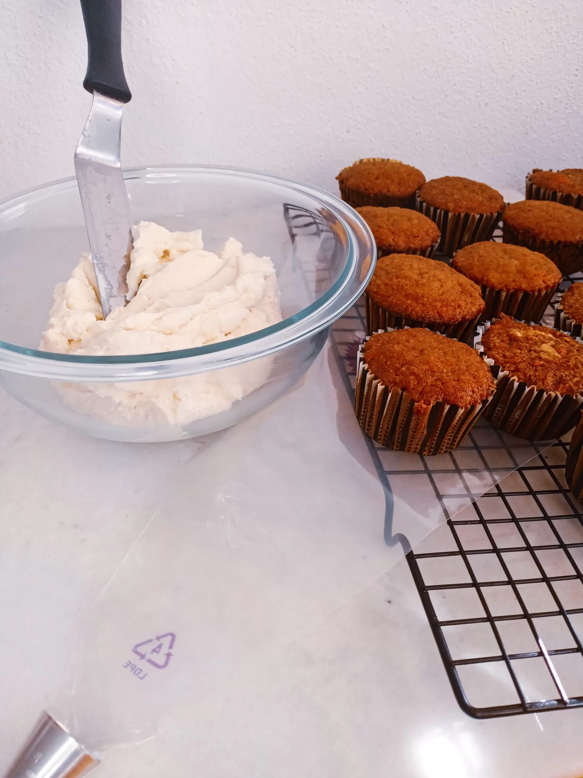 Keto sugar-free cream cheese frosting in a bowl with carrot cupcakes on a plate.