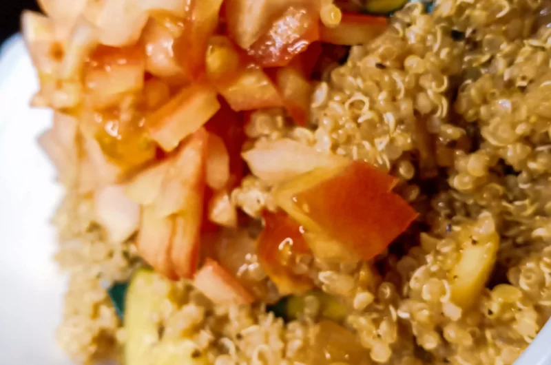 Zesty quinoa zucchini salad in a serving dish topped with fresh tomatoes.