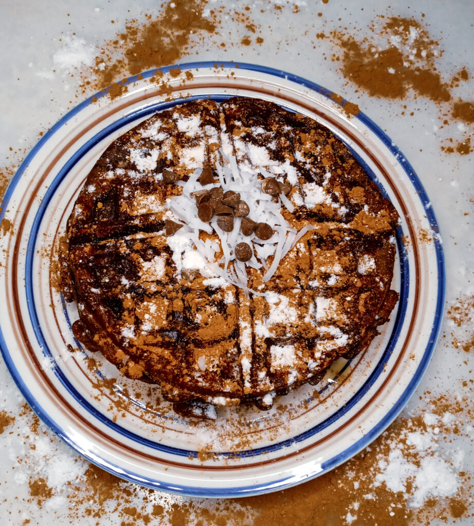 Keto chocolate protein waffles garnished with cacao powder, sugar-free powdered sugar, chocolate chips, and coconut