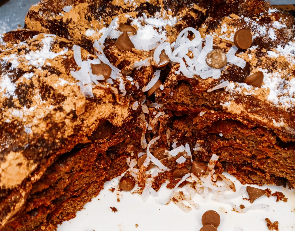 Keto chocolate protein waffles garnished with cacao powder, sugar-free powdered sugar, chocolate chips, and coconut