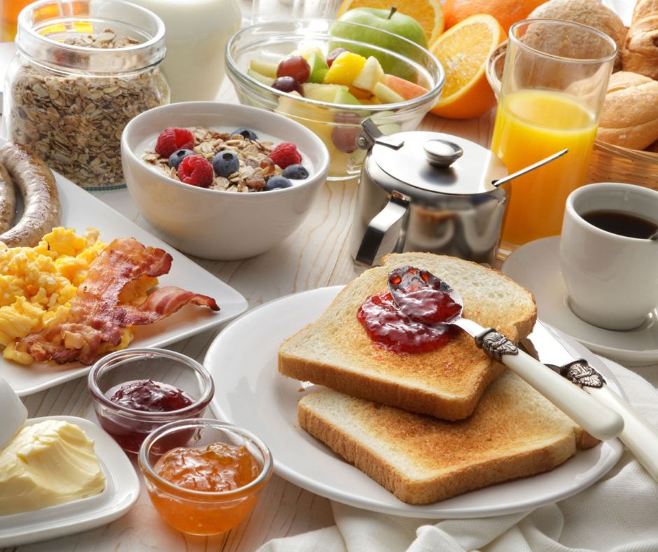 Breakfast spread with toast, jam, eggs, bacon sausage, granola, and yogurt bowl