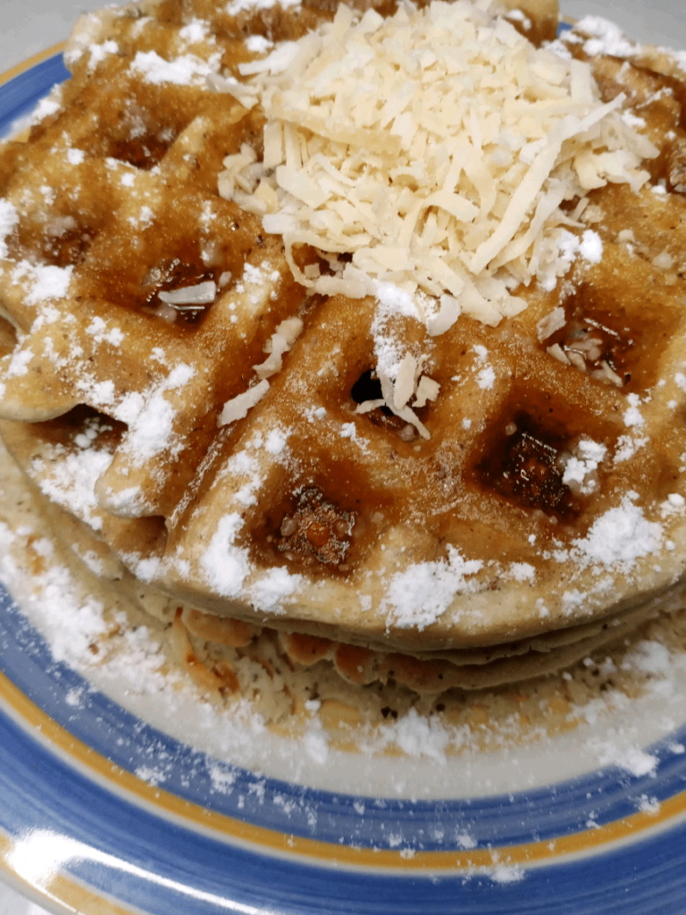Toasted coconut waffles on a plate topped with toasted coconut and sugar-free sweetener