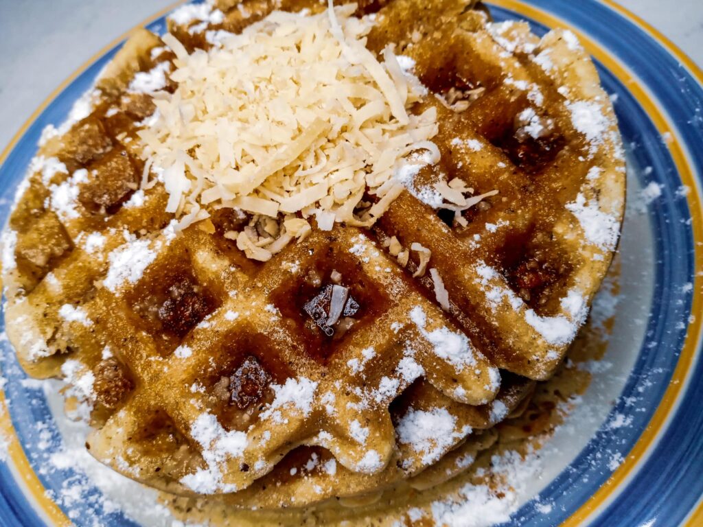 Toasted coconut waffles on a plate topped with toasted coconut and sugar-free sweetener