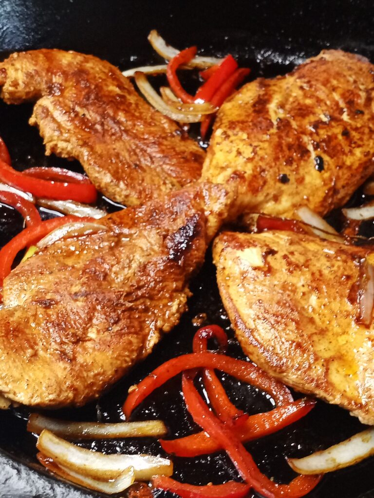Lemon paprika chicken breast in a cast-iron skillet with onions and peppers