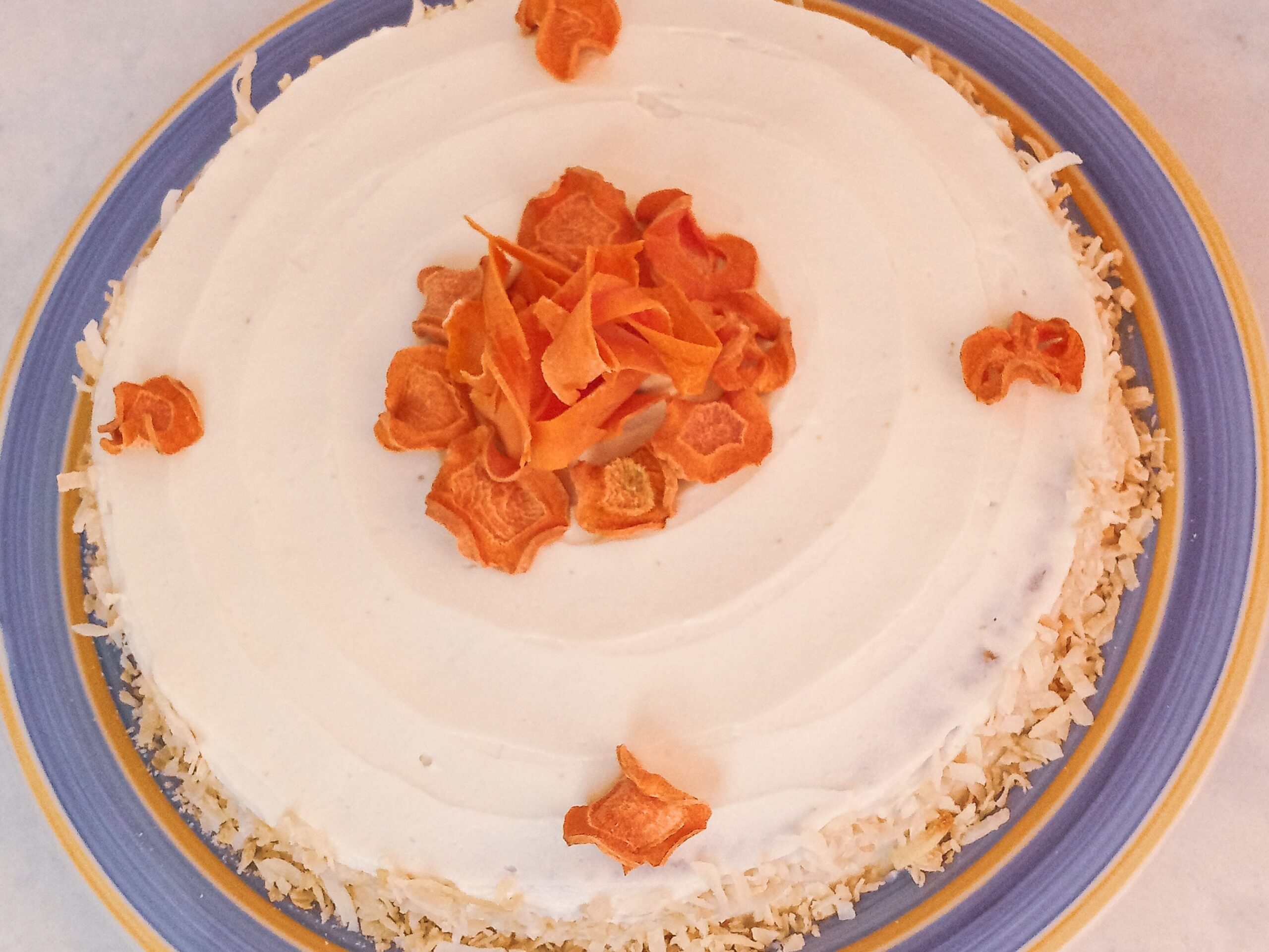 Gluten-free carrot cake decorated with sugar-free cream cheese frosting and dehydrated carrot chips on a plate.