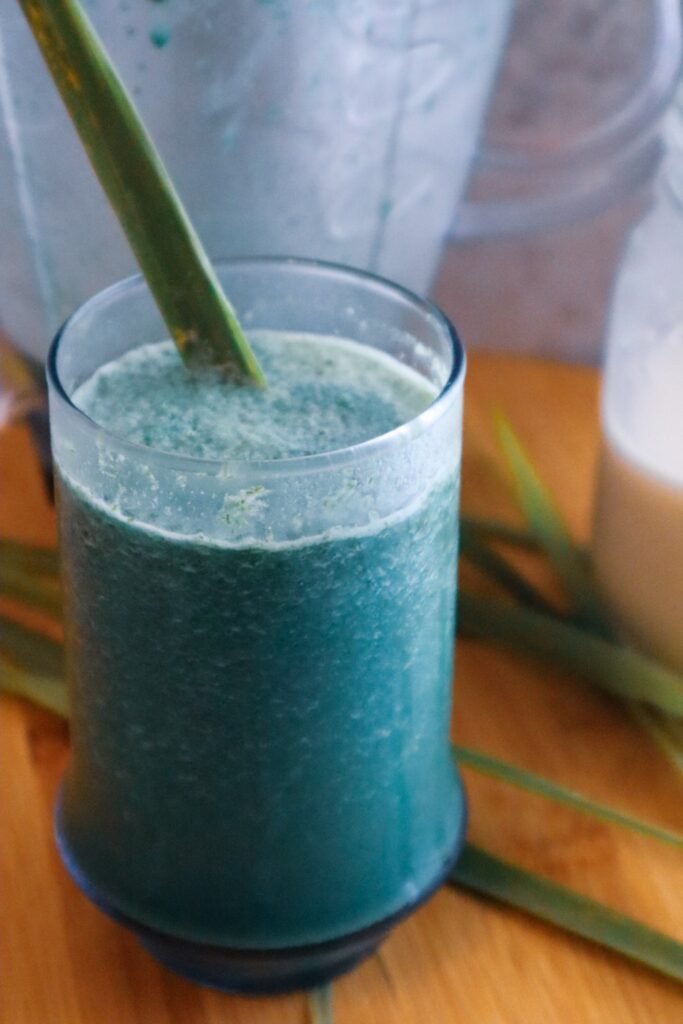 Fever grass green oat milk smoothie in a glass with a blender and oat milk in the background.