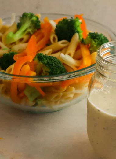Creamy Italian dressing in a jar with pasta salad in a bowl.