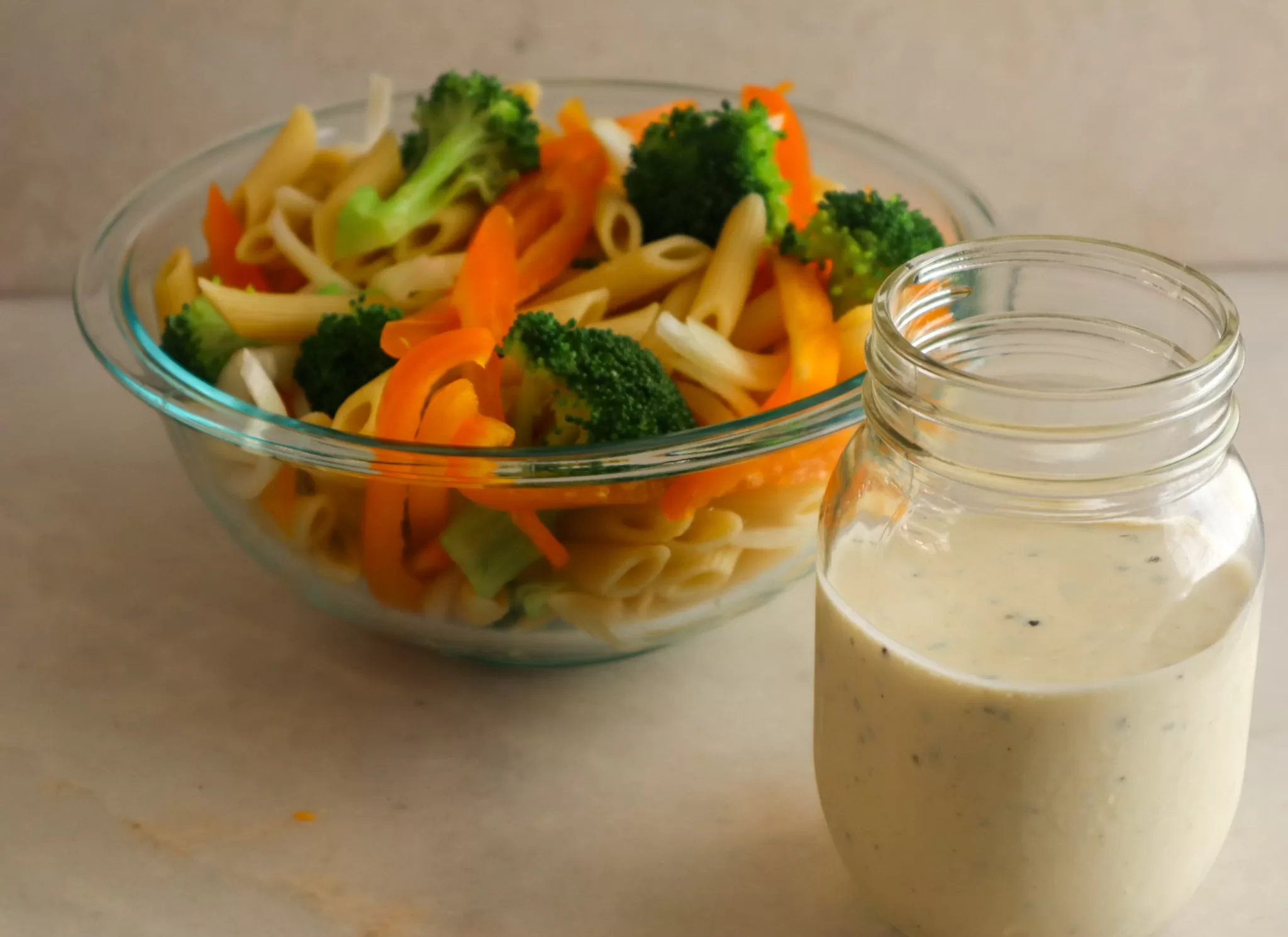 Creamy Italian dressing in a jar with pasta salad in a bowl.