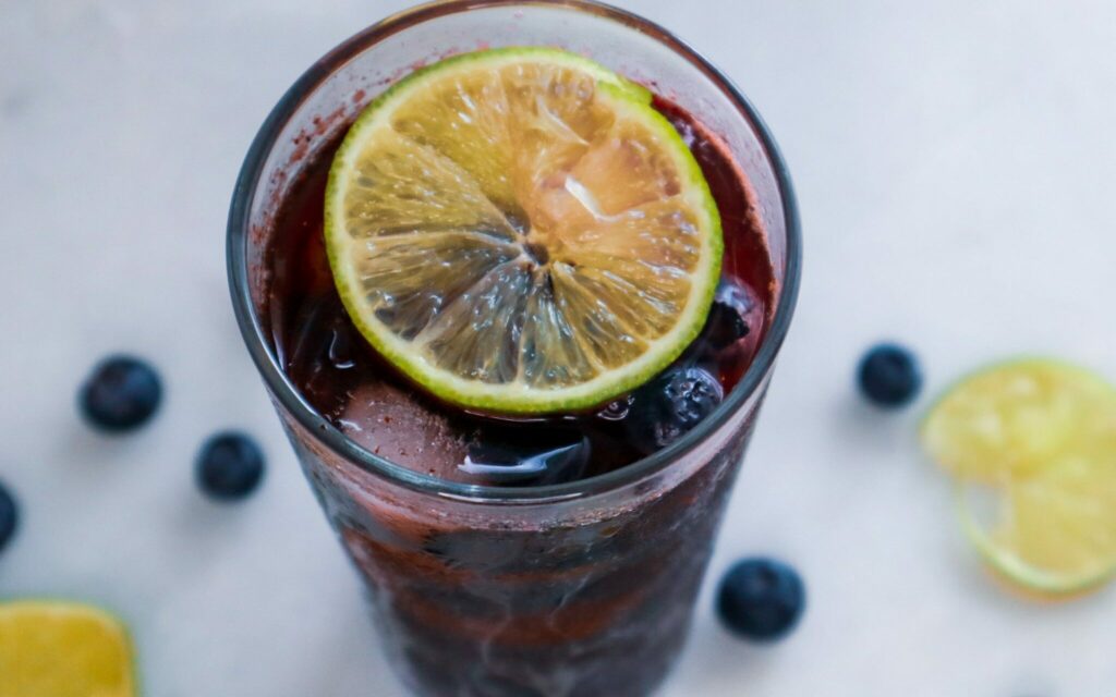 Odświeżacz Blueberry Lime w szklance ozdobionej plasterkami cytryny i jagodami.