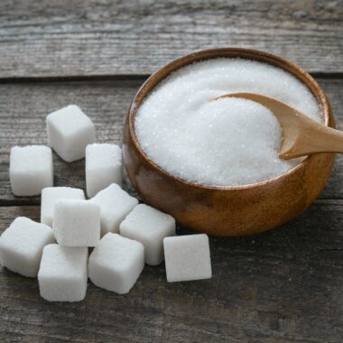 Granulated sugar in a bowl and sugar cubes on a photo board.
