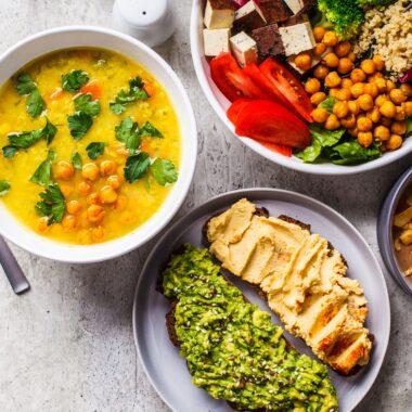 Chocolate smoothie bowl, lentil chickpea soup, tofu Buddha bowl, and toasts arranged on the countertop,