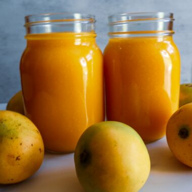 Mango puree in two Mason jars surrounded by fresh mangos.