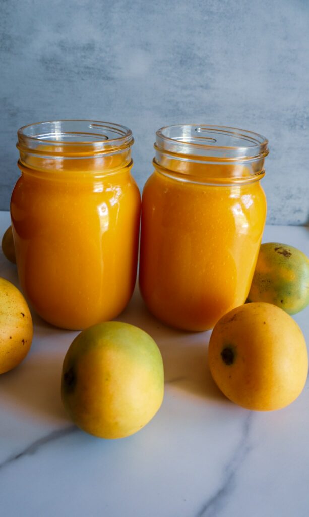 Mango puree in two Mason jars surrounded by fresh mangos.