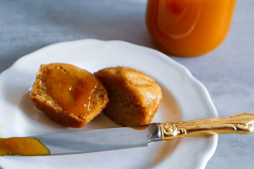 A mango muffin slathered with mango jam on a plate next to a jar of mango jam.