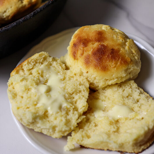 Gluten-free biscuits on a plate smeared with butter.