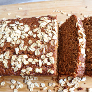 sliced oat flour applesauce bread on a cutting board garnished with oats.
