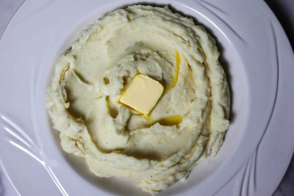 Garlic parmesan mashed potatoes in a serving bowl topped with a pat of butter.