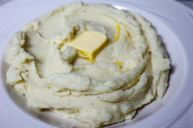 Garlic parmesan mashed potatoes in a serving bowl topped with a pat of butter.