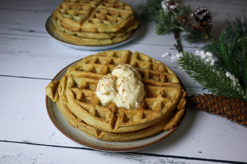 Gluten-free eggnog waffles on a plate topped with cream cheese frosting and sprinkled cinnamon.
