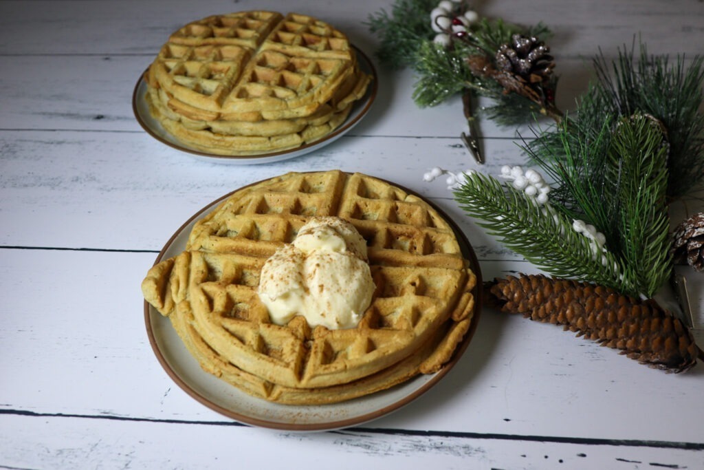 Gluten-free eggnog waffles on a plate topped with cream cheese frosting and sprinkled cinnamon.