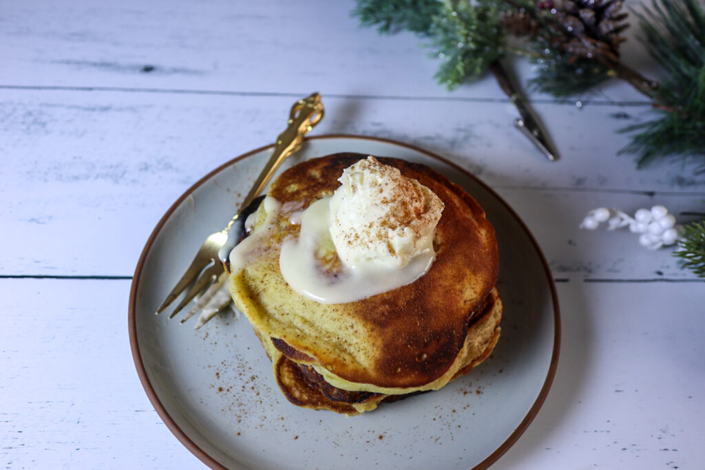 Gluten-free eggnog pancakes on a plate garnished with cream cheese frosting and cinnamon.