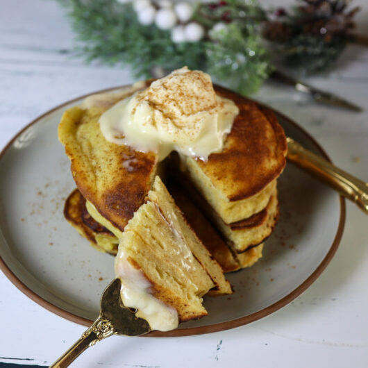 Gluten-free eggnog pancakes on a plate garnished with cream cheese frosting and cinnamon.