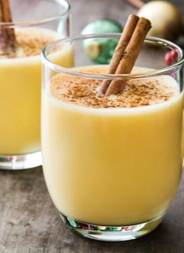 Eggnog in glasses garnished with nutmeg and cinnamon sticks.