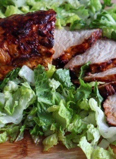 Air fryer BBQ pork tenderloin on a cutting board with fresh romaine lettuce.