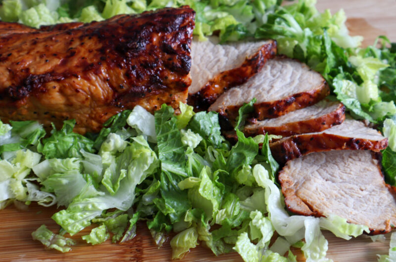 Air fryer BBQ pork tenderloin on a cutting board with fresh romaine lettuce.