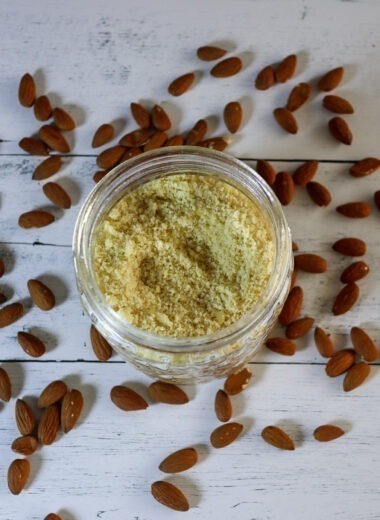homemade almond flour in a storage jar with whole almonds around it.