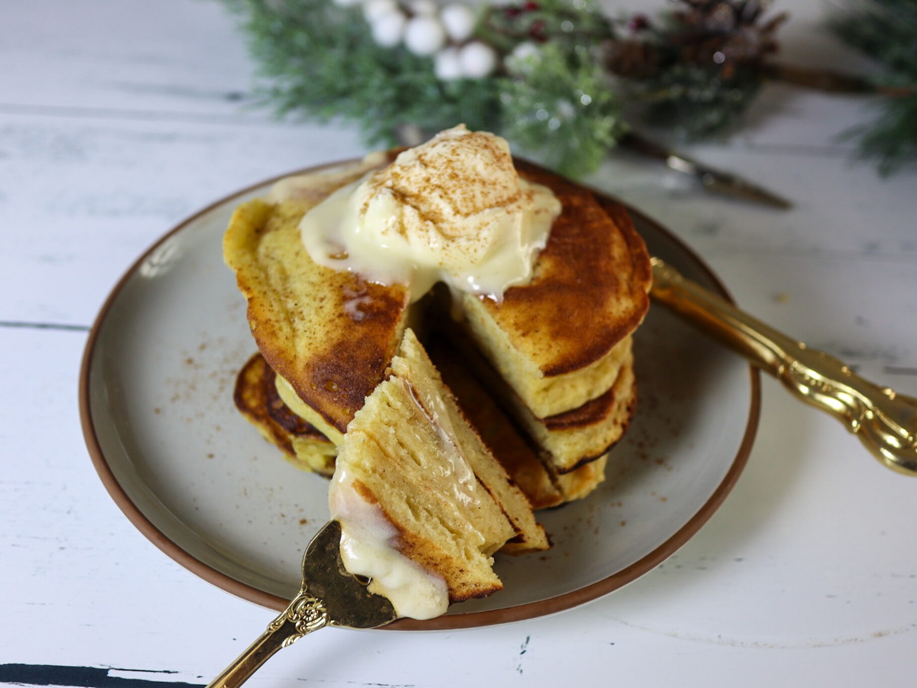Gluten-free eggnog pancakes on a plate garnished with cream cheese frosting and cinnamon.