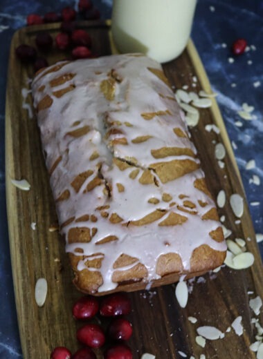 Christmas eggnog bread on a cutting board with fresh cranberries and sliced almonds.