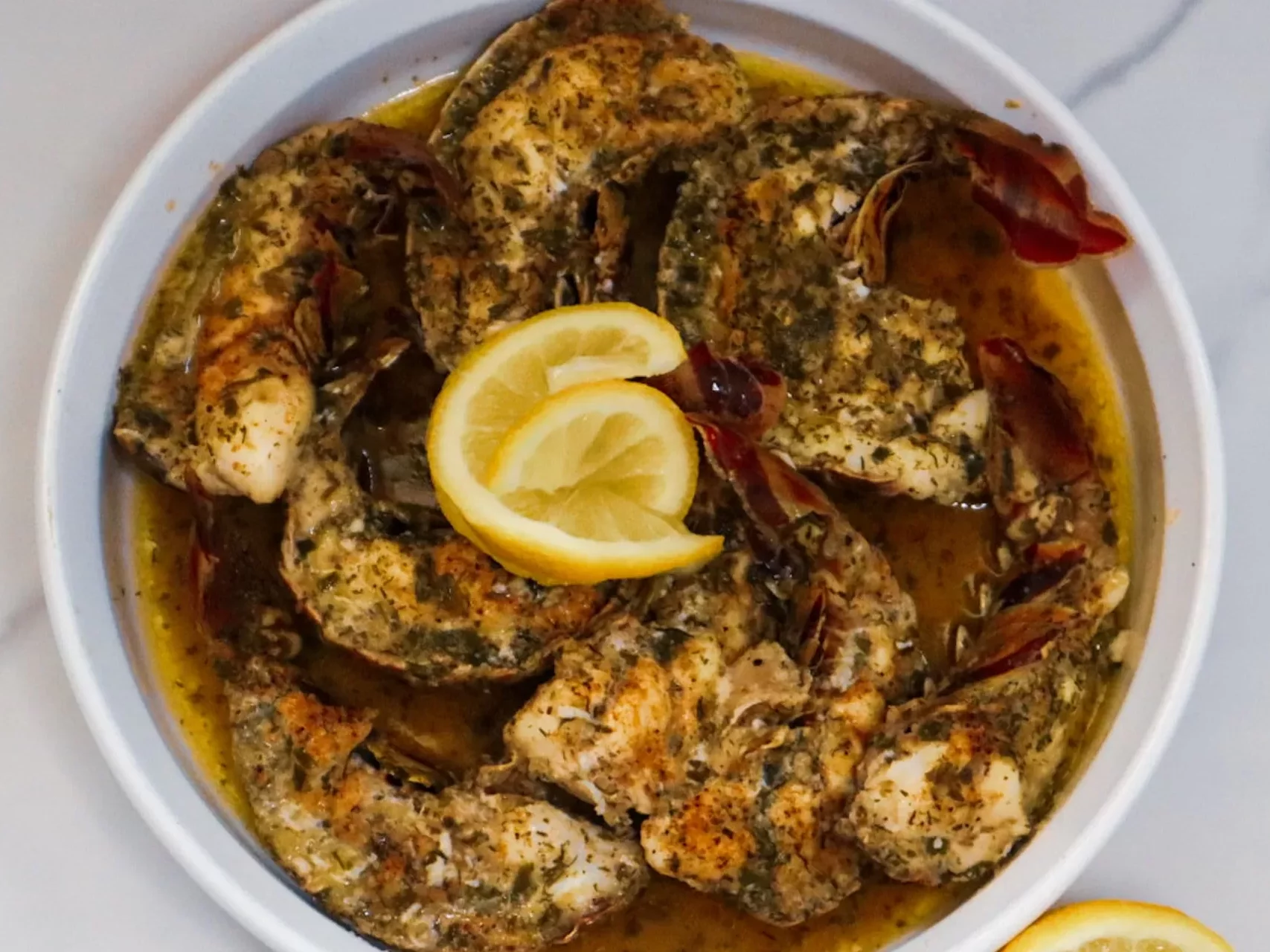 Baked garlic butter lobster tails in a baking dish garnished with lemon slices.