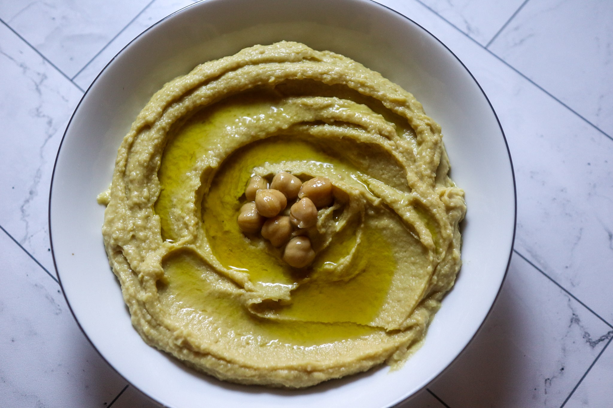 Homemade hummus in a serving bowl, garnished with olive oil and chickpeas.