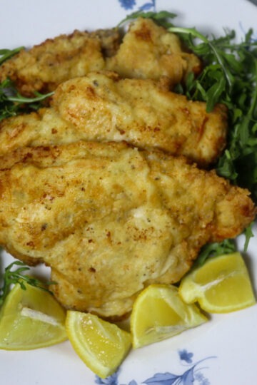 Breaded lemon pepper chicken garnished with lemon wedges and arugula.