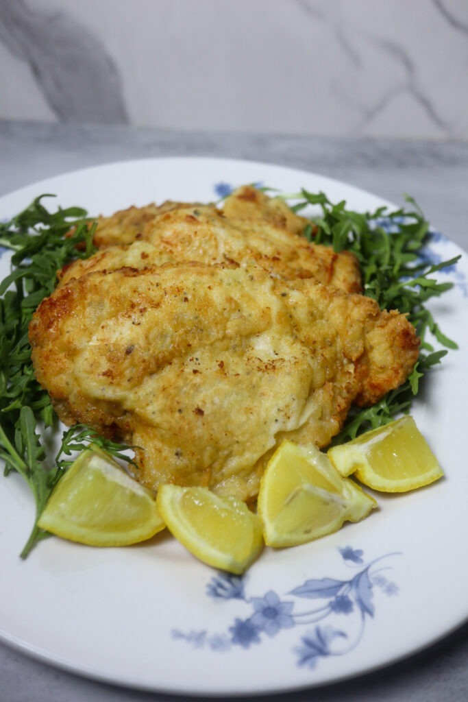Breaded lemon pepper chicken garnished with lemon wedges and arugula.