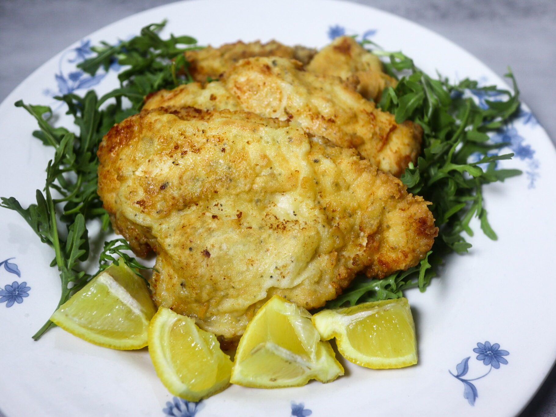 Breaded lemon pepper chicken garnished with lemon wedges and arugula.