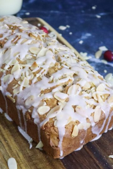 Eggnog bread on a cutting board garnished with sliced almonds and fresh cranberries.