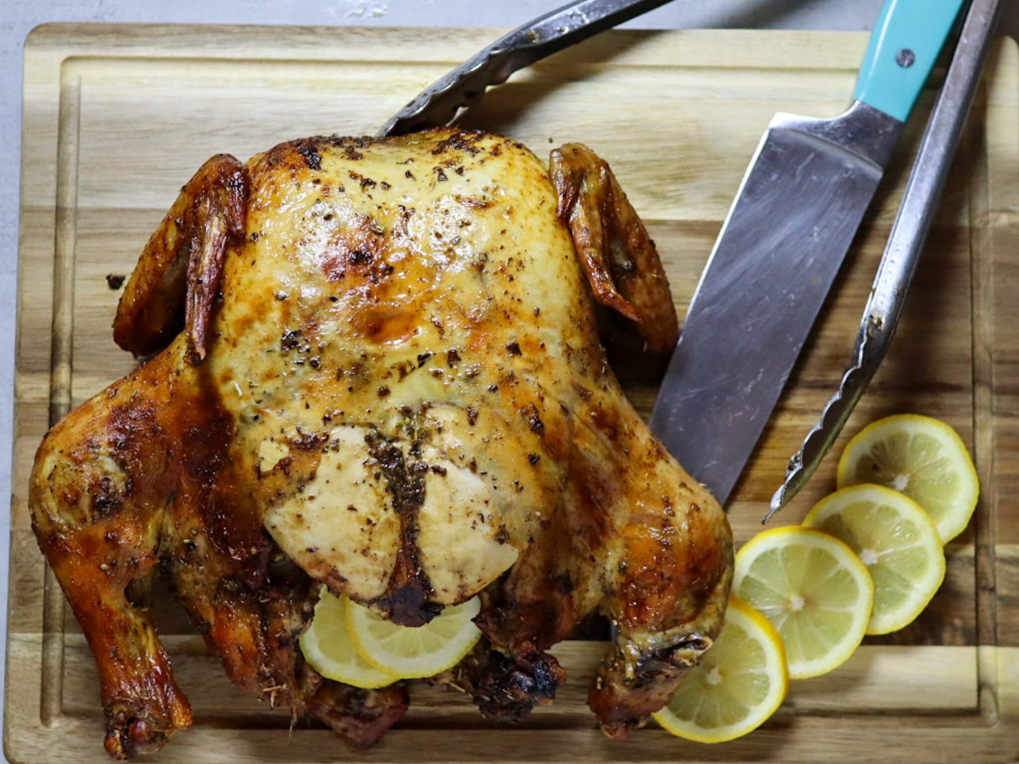 Lemon herb air fryer whole roasted chicken on a cutting board with fresh lemon slices.