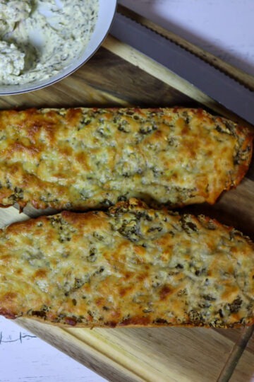 Cheesy garlic bread on a cutting board with garlic butter.